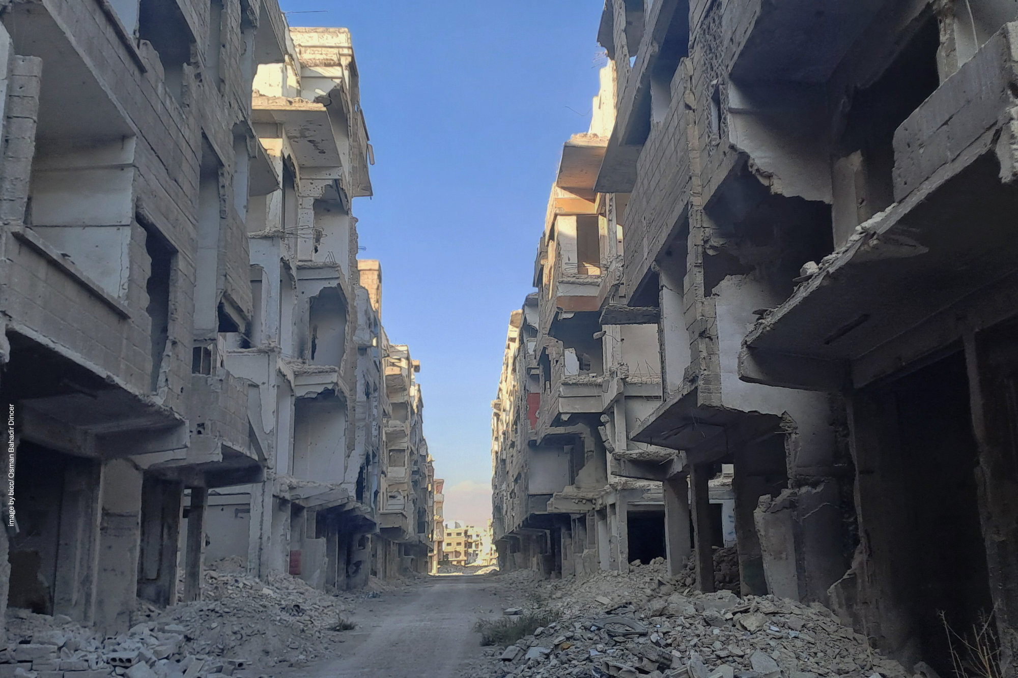 Ruined multi-story buildings lining a narrow street under a clear sky